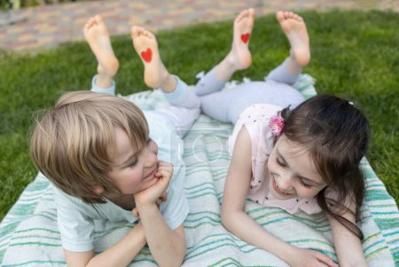Photo for Two cheerful children, a boy and a girl, lying on the green grass. happy childhood, children's love. positive atmosphere, tender feelings, friendship day. relax together on vacation - Royalty Free Image