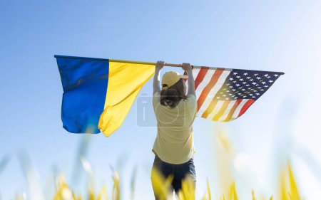 Photo for Woman on sunny day stands with back and raises up two large flags - American and Ukrainian. concept of cooperation and friendship . The United States is helping Ukraine win war with Russia - Royalty Free Image