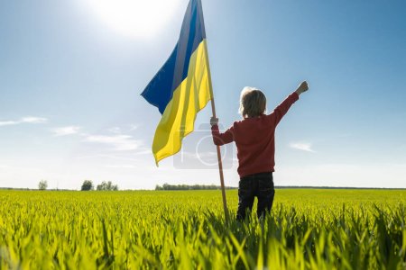 The Ukrainian flag flutters in the wind in the hands of a silhouette of a child standing on a green field on a sunny day. National symbol of freedom and independence. stop the war.