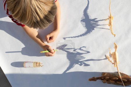 Kinderspuren mit einem Bleistift, die Schatten von den Skeletten von Spielzeug-Dinosauriern kontrastieren. Zeichnung eines Grundschülers, Leidenschaft für Paläontologie, Ideen für die Kreativität der Kinder