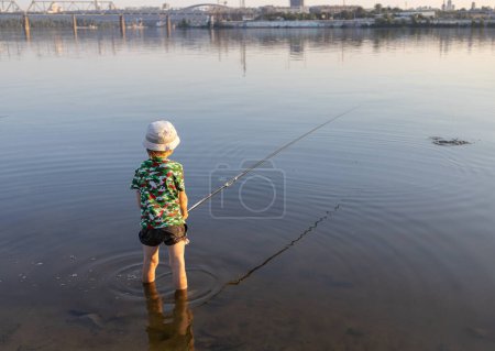 Téléchargez les photos : Garçon méconnaissable poissons debout avec des cannes à pêche dans l'eau de la rivière. concept de jour de pêche. passe-temps intéressant pour les vacances. Hobby pour un enfant - en image libre de droit
