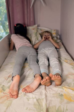 Two barefoot children lie next to each other on bed. Cozy morning of siblings. Selective focus on bare feet of boy and girl. relaxation, family joy, cute kids. brother sisters don't want to wake up