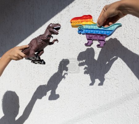 Foto de Juguetes de dinosaurios muestran interesantes sombras contrastantes en una pared de luz. Un día soleado brillante. feliz infancia alegre, ideas para juegos, estilo de vida - Imagen libre de derechos