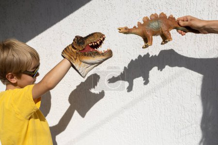Foto de Niño y mamá están jugando con dinosaurios de juguete, creando interesantes sombras contrastantes de ella en la pared. Un día soleado brillante. feliz infancia alegre, ideas para juegos, estilo de vida, desarrollo de la imaginación - Imagen libre de derechos