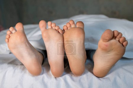 die nackten, sauberen Füße von zwei Kindern, Nachkommen, die nebeneinander unter derselben Decke auf dem Bett liegen. Morgenentspannung, gemütliche Erholung. Niedliche Bilder von Babyfüßen