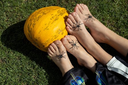 calabaza naranja y los pies desnudos de dos niños sobre los que están sentadas las arañas. Preparándose para Halloween. infancia alegre, mimos. No tengas miedo.