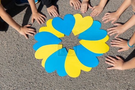 Foto de Corazones de papel en amarillo y azul y las manos de muchos niños alrededor en el día soleado. Acento de color. Los niños de Ucrania están en contra de la guerra. Día de la Independencia. Concepto patriótico. Unidad, orgullo de ser ucraniano - Imagen libre de derechos