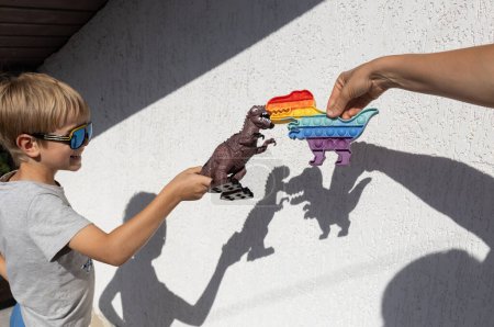 Foto de Adulto y niño juegan con sombras de juguetes de dinosaurios en la pared. interesantes sombras contrastantes. feliz infancia, ideas para juegos, estilo de vida, desarrollo de la imaginación. interés por la paleontología - Imagen libre de derechos