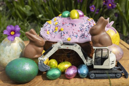 Photo for Model of a toy excavator, Easter cake, chocolate bunnies with bright multi-colored eggs. Easter spring holiday concept, greeting card from construction companies - Royalty Free Image