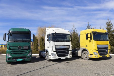 Foto de Tres camiones estacionados en fila en un día soleado. cabinas de diferentes colores de tractores-remolques. Vehículos comerciales, publicidad de automóviles para el transporte de negocios. Máquinas industriales de arrendamiento - Imagen libre de derechos