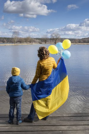 Téléchargez les photos : Civils, Ukrainiens, réfugiés, un petit garçon et une jeune femme avec un drapeau ukrainien bleu et jaune et des ballons. Famille, unité. Arrêtez la guerre. soutenir l'Ukraine. - en image libre de droit