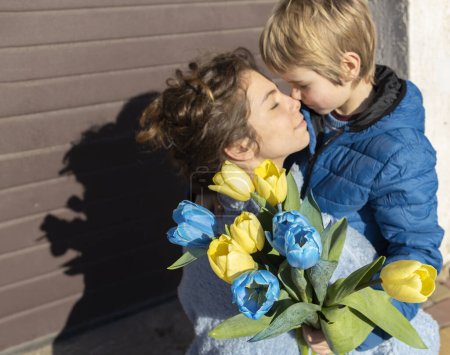 young woman and little boy out of focus . In the foreground is a bouquet of blue and yellow tulips. Long-awaited meeting. Family, unity, consolidation. take care and support each other during the war