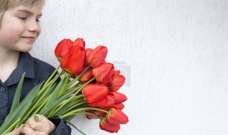 bouquet of red tulips on a light background and the face of a cute boy in profile. copy space. Mother's Day, Valentine's Day, hi spring