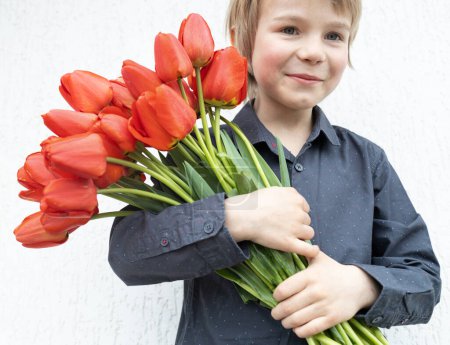 gran ramo de tulipanes rojos en las manos de un alegre niño de 6 años. Día de San Valentín. Día de las Madres. Regalo de flores con amor. joven caballero. enfoque selectivo.