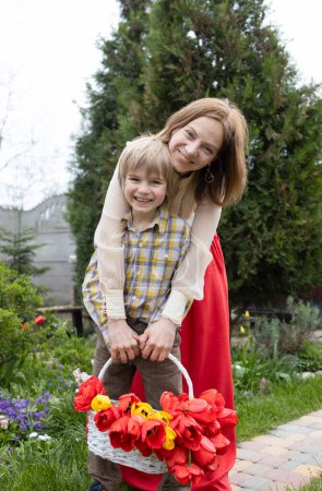 Porträt eines niedlichen 6-jährigen Sohnes und einer Mutter mit einem Strauß Tulpen in einem Korb. Muttertag, Geburtstag. Die Atmosphäre der familiären Liebe und Positivität. Glückliche Mutterschaft