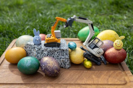 Osterferienkonzept. Postkarte von Baufirmen. Spielzeugmodelle von Baumaschinen - Bagger und gefärbte Eier