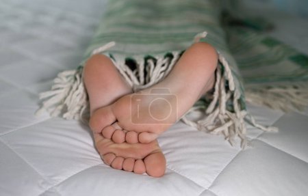 primer plano de los pies desnudos lindo de un niño envuelto en una manta acostada en la cama. Buenos días, perezoso. Acogedor lugar para dormir, dormir con placer, ternura infantil, pies sanos