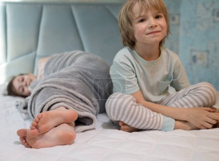 Foto de Dos niños descalzos en pijama, hermano y hermana, juegan en la cama en casa. mimos familiares de niños por la mañana o por la noche. La infancia alegre de la descendencia, el descanso confortable. enfoque selectivo - Imagen libre de derechos