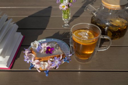 bread toast with spring flowers, a glass cup of tea and a teapot - a beautiful healthy breakfast. Pages of an open book on a table on a sunny day. good morning, floral fantasies, relaxing atmosphere