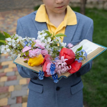 bouquet of spring flowers lie on pages of open book held by child. Time for relaxation and education. Cozy poetic atmosphere. gift for mom on Mother's Day. good morning, floral fantasy. back to school