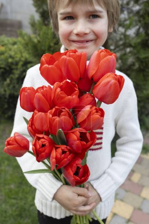 Junge 7 Jahre alt mit einem Strauß roter Tulpen. Alles Gute zum Muttertag, alles Gute zum Geburtstag. Positive Atmosphäre, Dankbarkeit, mit Liebe. Selektiver Fokus
