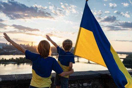 Maman et son fils avec le drapeau ukrainien se tiennent haut sur le toit sur le fond du ciel et de la rivière Dniepr à Kiev. Patriotisme, attirant l'attention sur la guerre en Ukraine. Jour de l'indépendance.