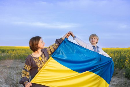 Porträt einer ukrainischen Familie, Mutter und Sohn mit blau-gelber Flagge vor dem Hintergrund eines blühenden Rapsfeldes. Der ukrainische Unabhängigkeitstag. die Ukraine zu unterstützen. Stoppt den Krieg