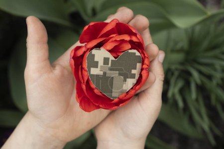 large red flower and heart cut out of camouflage military fabric on child's palms. Stop war. With love and gratitude to soldiers of Armed Forces. a symbol of memory of soldiers who died in the war