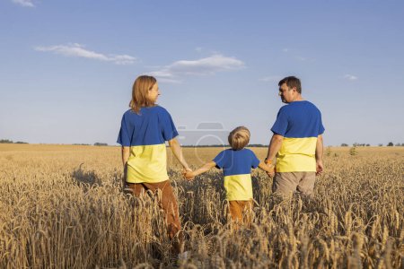 Ukrainische Familie in identischen gelben und blauen T-Shirts steht zwischen Ähren auf dem Feld. Schluss mit dem Krieg. Stolz auf die Nation, Unterstützung, Siegesglauben. Der ukrainische Unabhängigkeitstag. Wert des Getreides