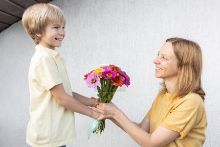 Atmosphäre familiärer Liebe und Positivität. Glückliche Mutterschaft. Sohn schenkt seiner geliebten Mutter einen Blumenstrauß zum Muttertag oder Geburtstag.