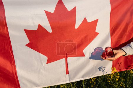 Rotes Herz in der Hand einer Frau auf dem Hintergrund der kanadischen Flagge. Tag der kanadischen Unabhängigkeit. Stolz, Freiheit, Vaterlandsliebe. Patriotismus. Reisen durch das Land