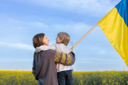 Familia ucraniana, madre e hijo con una bandera azul y amarilla entre un campo de colza floreciente. Día de la Independencia de Ucrania. apoyar a Ucrania en la confrontación con Rusia. Detener la guerra