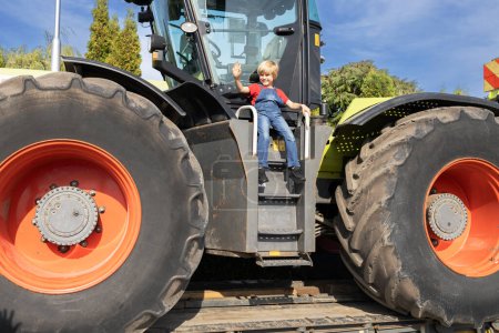 child sits happily on a huge farm tractor. Equipment for agriculture and agribusiness. The boy's interest in machines and their work. Men's hobbies