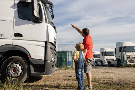 boy and a man, against the background of trucks, are enthusiastically looking at the cars. Spend the day with your son. The boy's interest in machines and their work. Father's Day