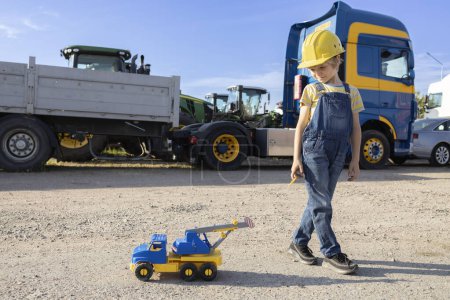 7-year-old boy plays with a toy car, and behind him are large cabins of commercial vehicles. interesting childhood of a child, games in the profession. The boy's interest in machines and their work.