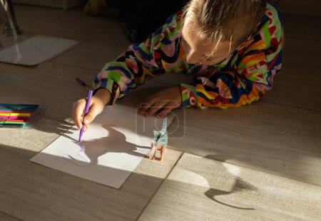 child draws contrasting shadows from a toy dinosaur standing on the floor, illuminated by the sun. drawing by a primary school student, ideas for creativity. Interesting activities for children