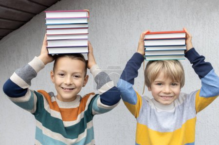 Zwei fröhliche, lustige 8-jährige Jungen halten einen Stapel Bücher auf ihren Köpfen. zurück zur Schule. Tag des Buches. Lesen Sie mit Vergnügen. Konzept von Lesen, Bildung, Weisheit, Wissen. Digitale Entgiftung