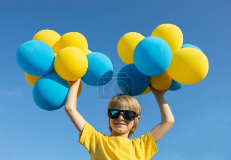 garçon tient de nombreux ballons jaunes et bleus au-dessus de la tête sur le fond du ciel. couleurs du drapeau ukrainien. Jour de l'indépendance de l'Ukraine. Le jour du ballon. Anniversaire. Moment lumineux de l'enfance heureuse