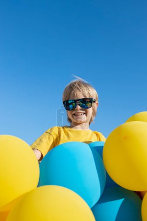 visage d'un enfant derrière de nombreux ballons jaunes et bleus sur le fond du ciel par une journée ensoleillée. désir de paix pour l'Ukraine. Je suis fier d'être ukrainien. bonne humeur, anniversaire