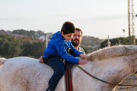 Photo for Boy with disabilities riding a horse during an equine therapy session with a male instructor. People with disability. - Royalty Free Image