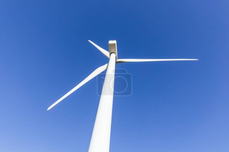 tiro de bajo ángulo de una turbina eólica, que simboliza la generación de electricidad limpia y sostenible. Con un cielo azul vibrante como telón de fondo, la imagen destaca el poder y la belleza de las renovables