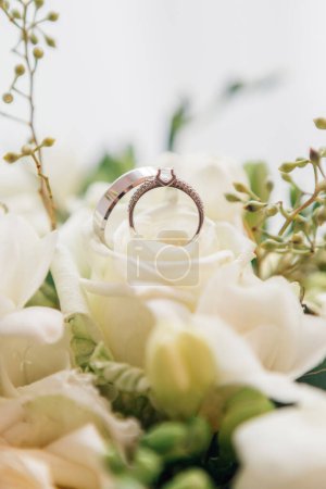 Foto de Los anillos de boda se encuentran en un hermoso ramo como accesorios nupciales. Vista de cerca de los anillos de boda dorados y hermosas flores azules pequeñas en la mesa de madera - Imagen libre de derechos