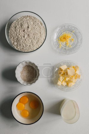 Téléchargez les photos : Culinary flat lay with ingredients for cozonac dough. Top view on table with bowl of flour,  yeast, butter, eggs, milk and lemon rind. Traditional Romanian recipe preparation. Healthy food lifestyle. - en image libre de droit