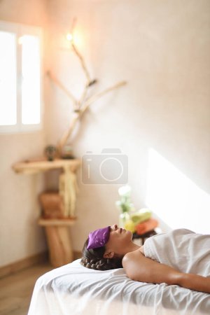 Photo for Woman lying with towel on stretcher waiting for the start of her massage and facial treatment in vertical plane and copy space. - Royalty Free Image