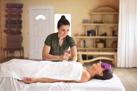 Photo for Female masseur giving massage to woman lying down and relaxing in therapy salon interior - Royalty Free Image