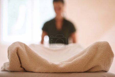 Photo for Massage session with towel covered body in foreground and masseuse figure in blurred background. - Royalty Free Image