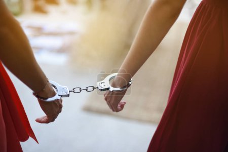 Photo for Two handcuffed women, dressed in red in close-up and blurred background, conceptual image. - Royalty Free Image