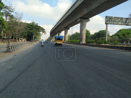 Téléchargez les photos : Bangalore, Karnataka / Inde-20 avril 2020 : Gros plan de la magnifique route d'asphalte de Bangalore avec le pont du métro Namma ou le survol d'un côté près du Goraguntepalya. En raison de Covid 19 Lock down Road est vide. - en image libre de droit