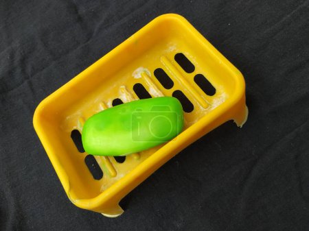 Téléchargez les photos : Gros plan de savon de bain de couleur verte utilisé dans une boîte en plastique de couleur orange isolé sur un fond noir - en image libre de droit