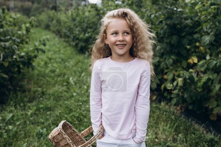 Téléchargez les photos : Petite fille aux cheveux blonds et aux yeux bleus joue joyeusement dans le jardin, apprécie la nature et l'air pur. Santé et joie des enfants. Bonne enfance - en image libre de droit